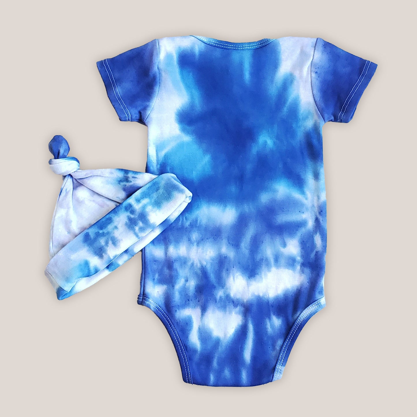 A blue and white tie dye baby bodysuit with a matching hat.