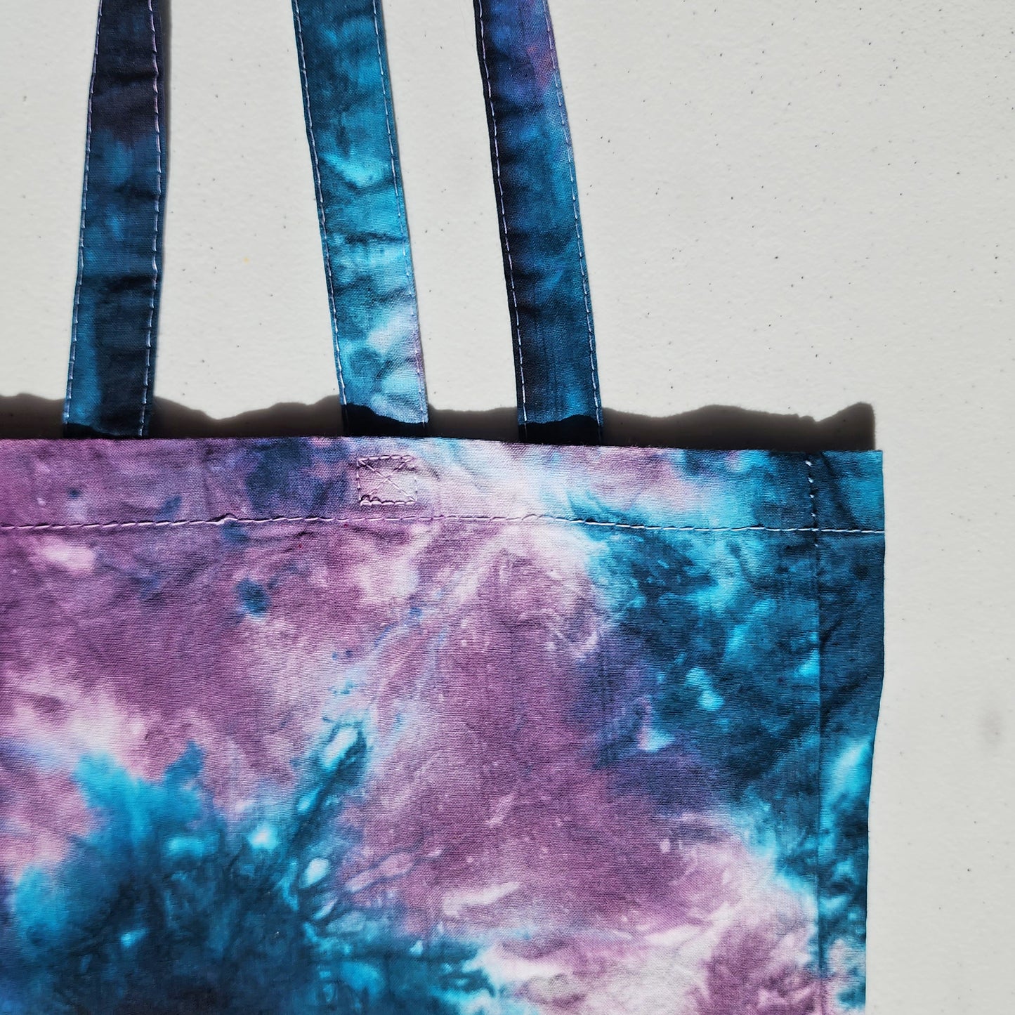 Tie-dye tote bag with blue and purple handles on a light gray background