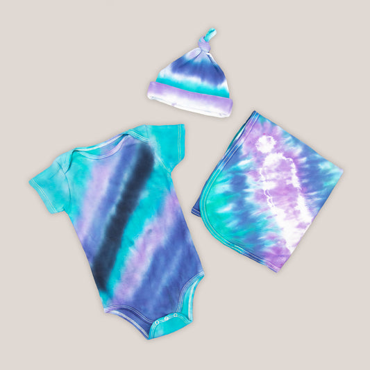 Teal, purple, and black tie dye baby set that includes a baby hat, bodysuit, and baby blanket.