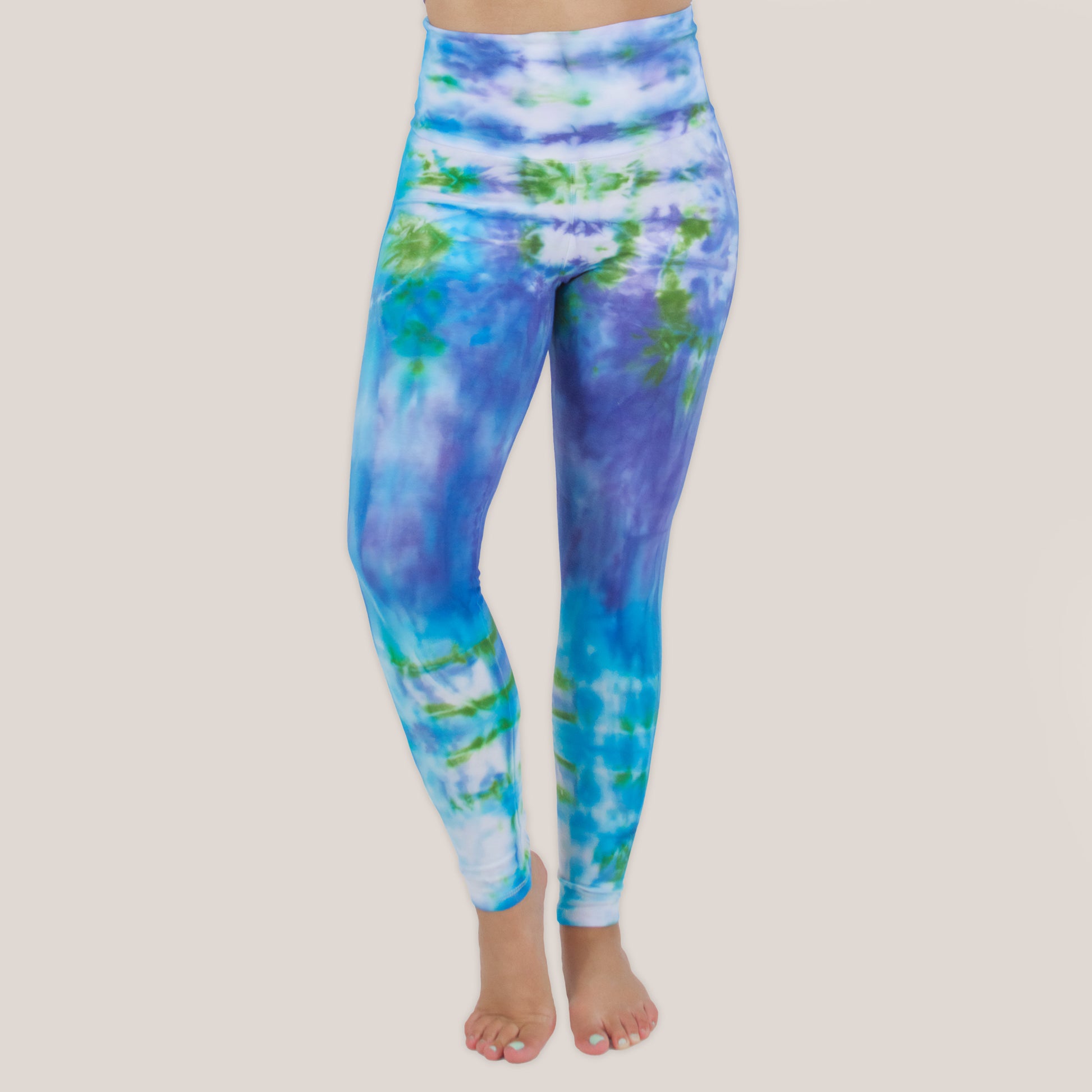 Woman wearing the Grenada tie dye leggings that feature a fold over waistband.  The colors of the leggings include aqua, lavender, and emerald by Akasha Sun