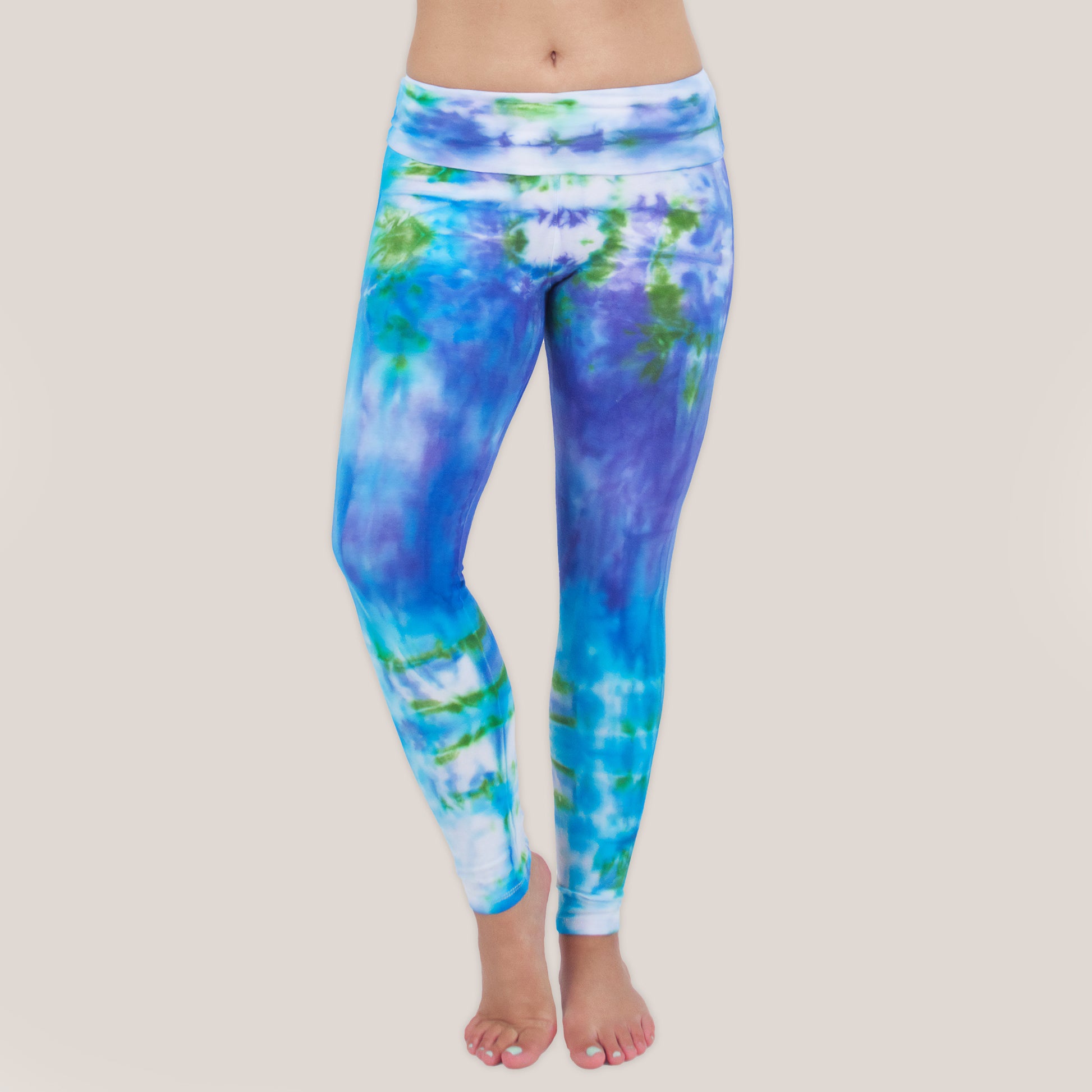 Woman wearing the Grenada tie dye leggings that feature a fold over waistband.  The colors of the leggings include aqua, lavender, and emerald by Akasha Sun