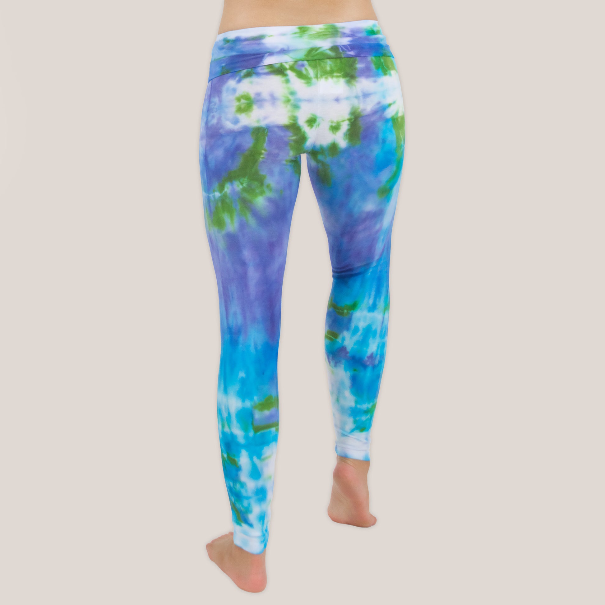 Woman wearing the Grenada tie dye leggings that feature a fold over waistband.  The colors of the leggings include aqua, lavender, and emerald by Akasha Sun