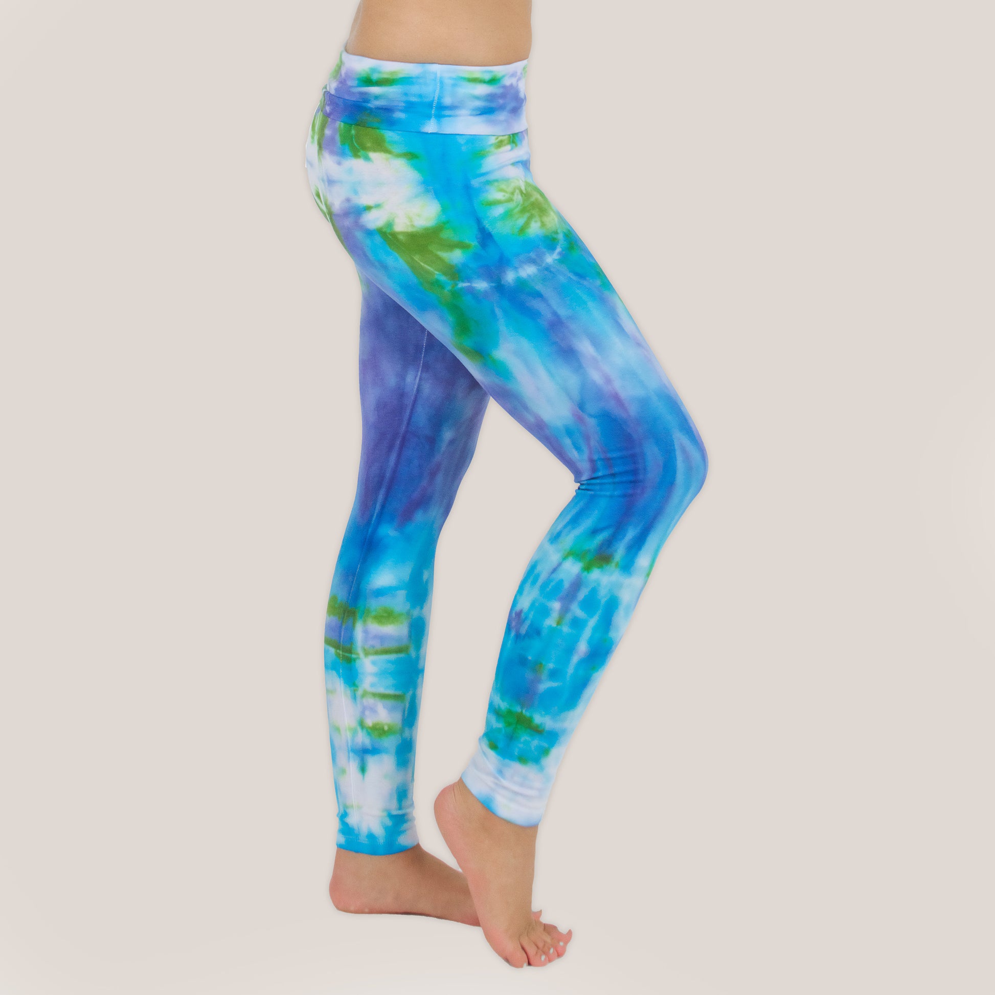 Woman wearing the Grenada tie dye leggings that feature a fold over waistband.  The colors of the leggings include aqua, lavender, and emerald by Akasha Sun