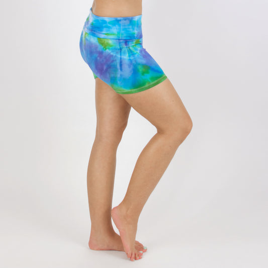 Woman wearing the Grenada tie dye shorts featuring a fold over waistband. The colors in the shorts include blue, purple, and green by Akasha Sun