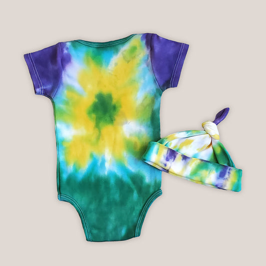An organic tie dye baby bodysuit and hat in Mardi Gras colors of green, purple, and yellow.