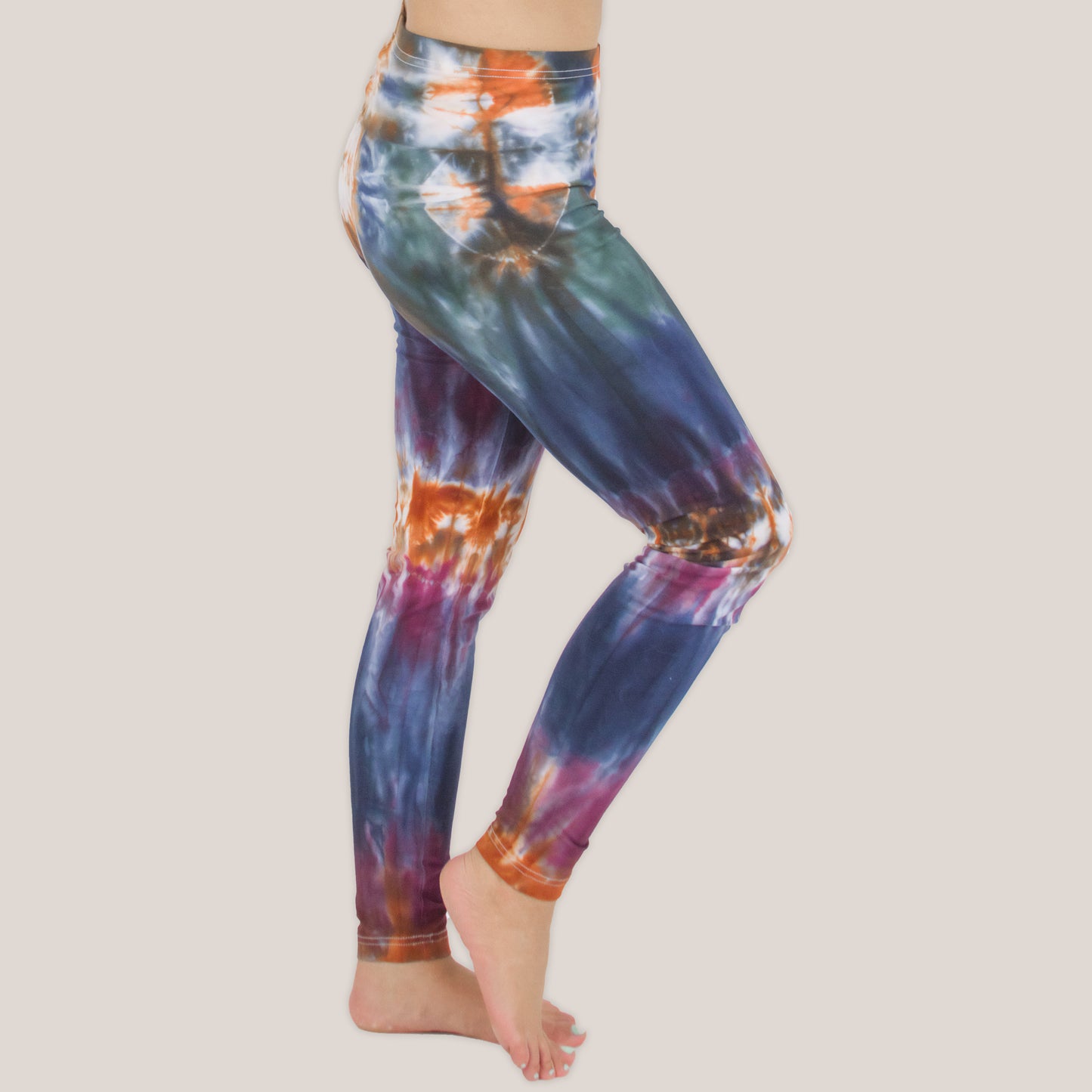 Woman wearing the Meteor tie dye leggings that feature the hues orange, navy, purple, and green by Akasha Sun