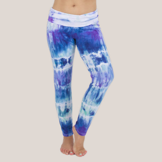Woman wearing the Mykonos tie dye leggings featuring a fold over waistband.  The colors in the pants include blue, light teal, purple, and white by Akasha Sun