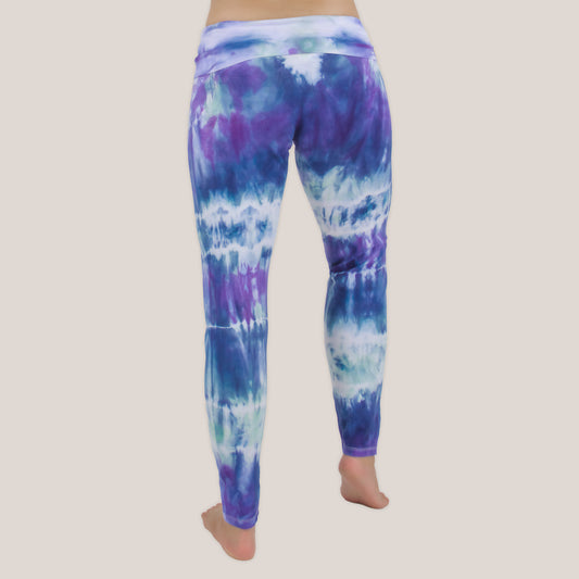 Woman wearing the Mykonos tie dye leggings featuring a fold over waistband.  The colors in the pants include blue, light teal, purple, and white by Akasha Sun