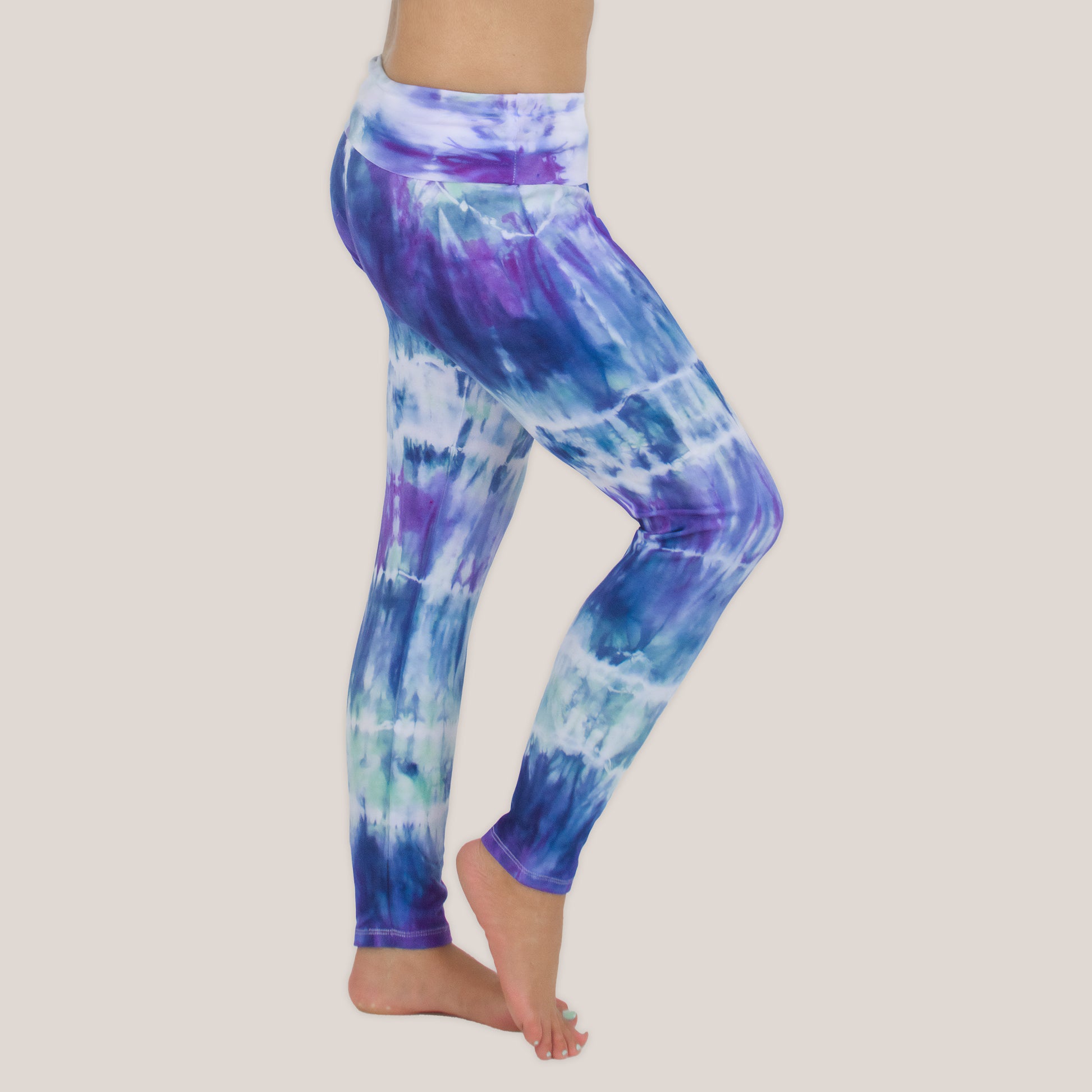 Woman wearing the Mykonos tie dye leggings featuring a fold over waistband.  The colors in the pants include blue, light teal, purple, and white by Akasha Sun