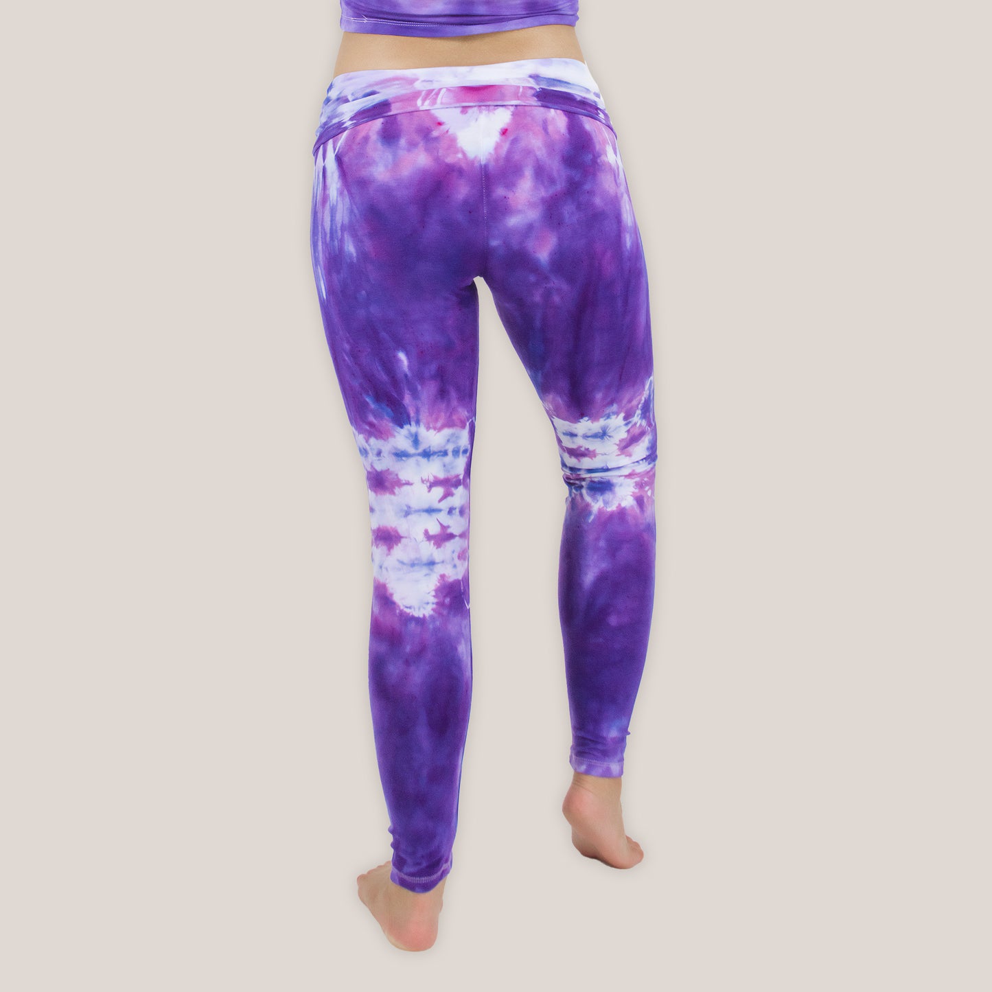 Woman wearing the Saint-Tropez tie dye leggings that feature a fold over waistband. The colors in these pants include purple, pink, and white.