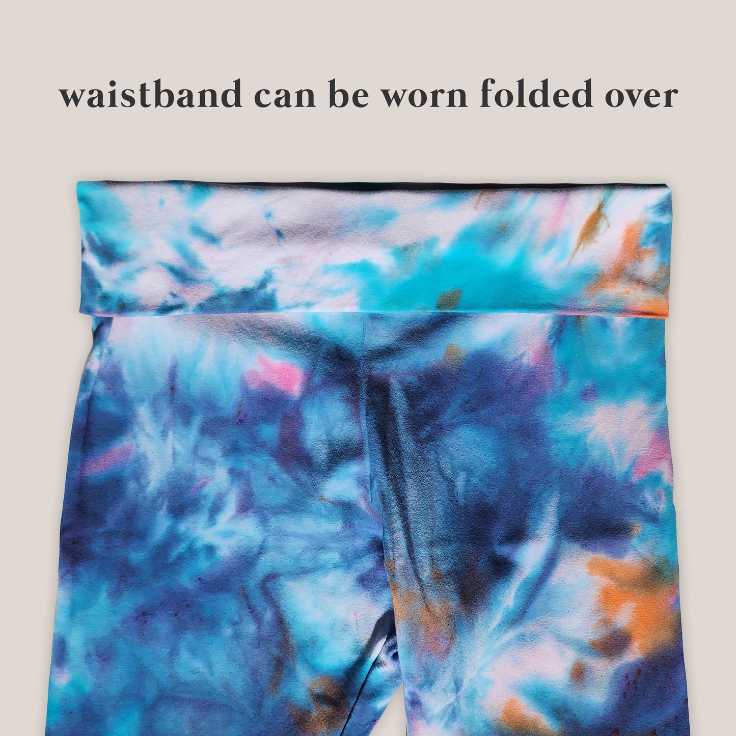 Colorful tie-dye leggings with a waistband that can be folded over on a beige background.