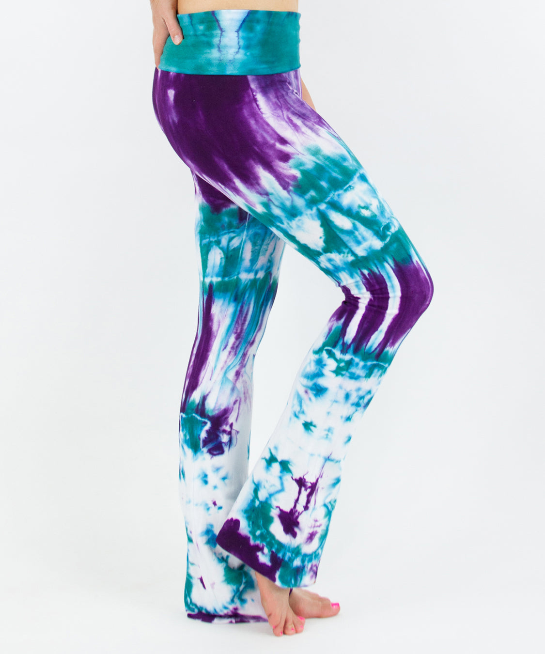 Woman wearing a pair of teal and purple tie dye yoga pants featuring a fold over waistband.