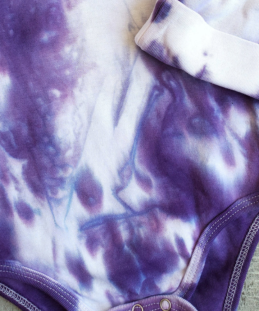 A purple and white tie dye baby bodysuit.