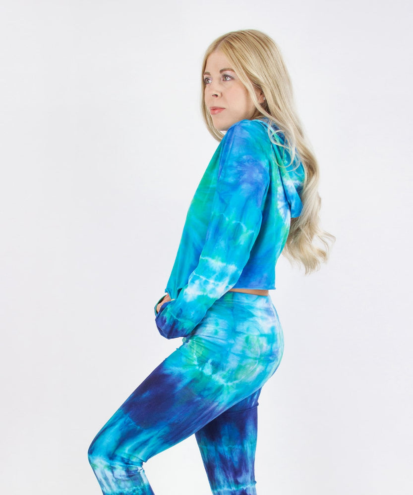 Woman wearing the Galapagos Islands Tie Dye Hoodie Crop Top.  The colors of the crop top include navy blue, teal, aqua, and blue.  Featuring a hood, drawstrings, and raw edge.
