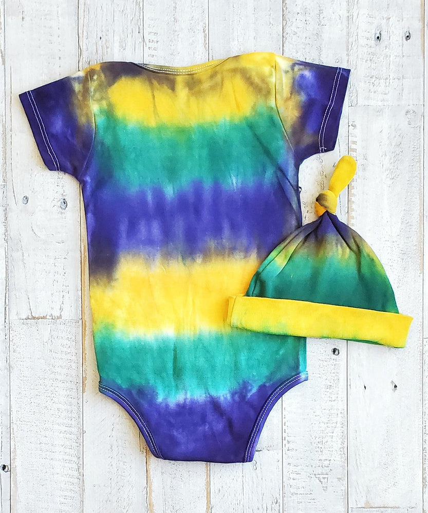 A tie dye organic baby set including a baby blanket bodysuit, hat, and blanket in Mardi Gras colors.