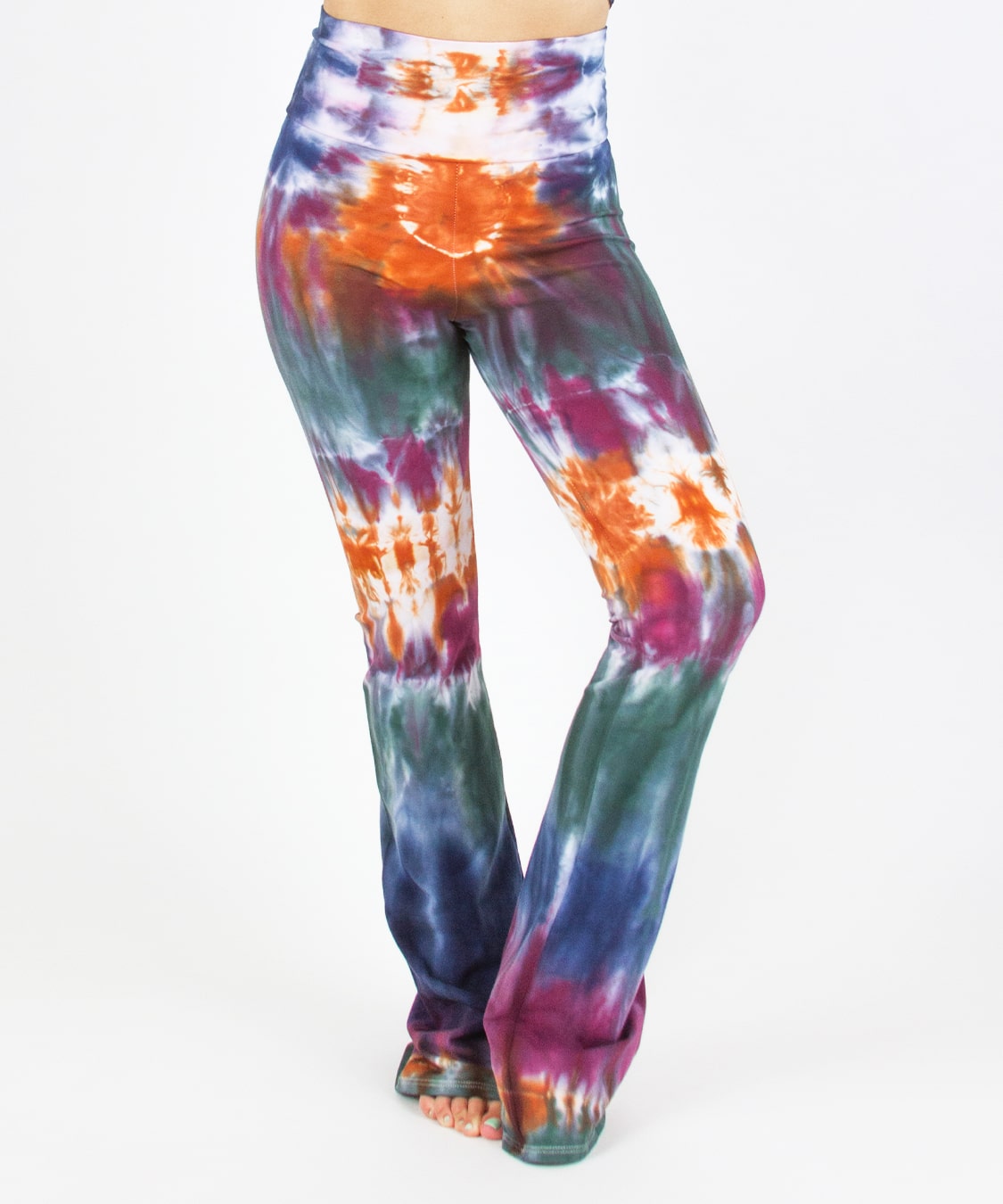Woman wearing the Meteor tie dye yoga pants that feature a fold over waistband. The colors in these pants include orange, purple, green, and navy blue.