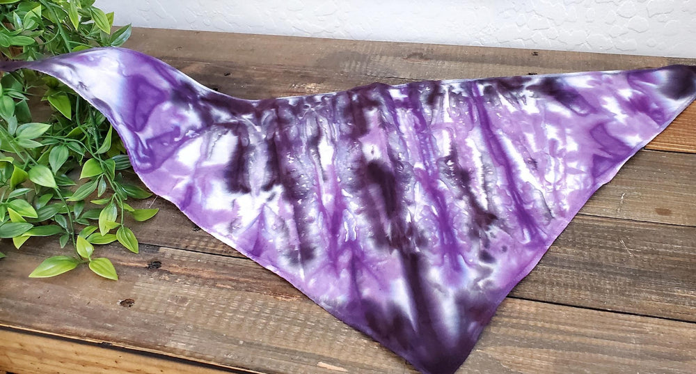 A dog modeling a tie dye dog bandana in the colors purple and black.