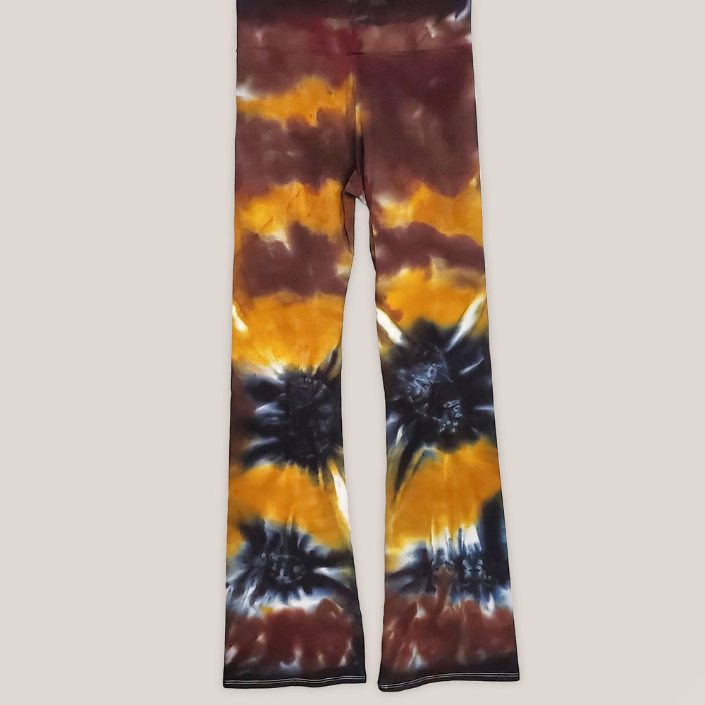 A pair of tie dye yoga pants with a wide waistband in the color amber, brown, and black.