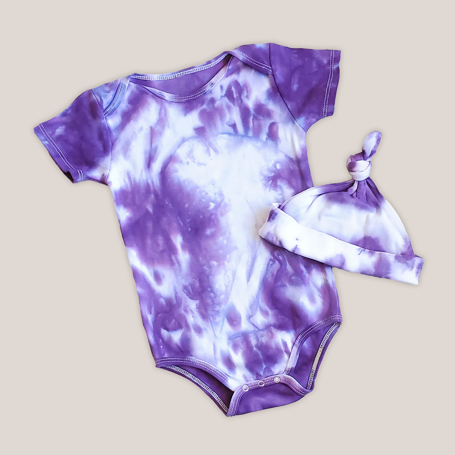 A purple and white tie dye baby bodysuit.