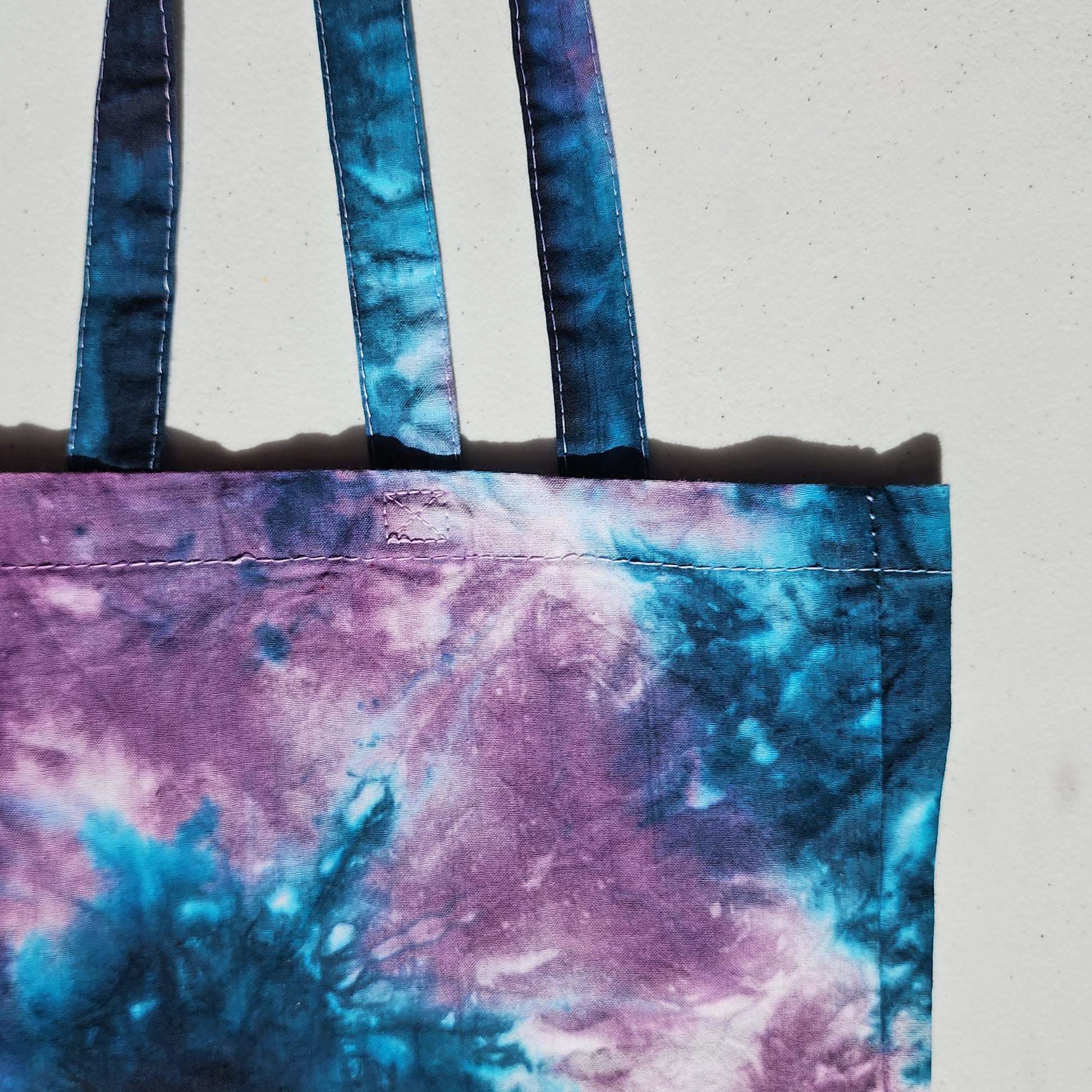 Tie-dye tote bag with blue and purple handles on a light gray background