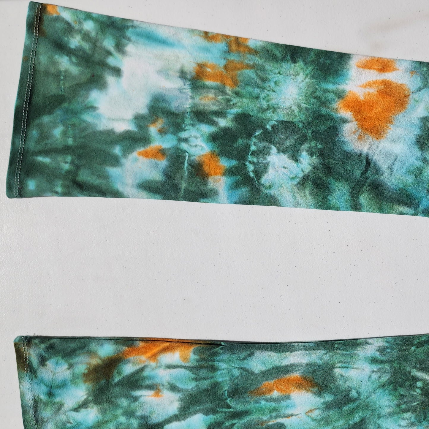 Tie-dye patterned pants with green and orange colors on a white background