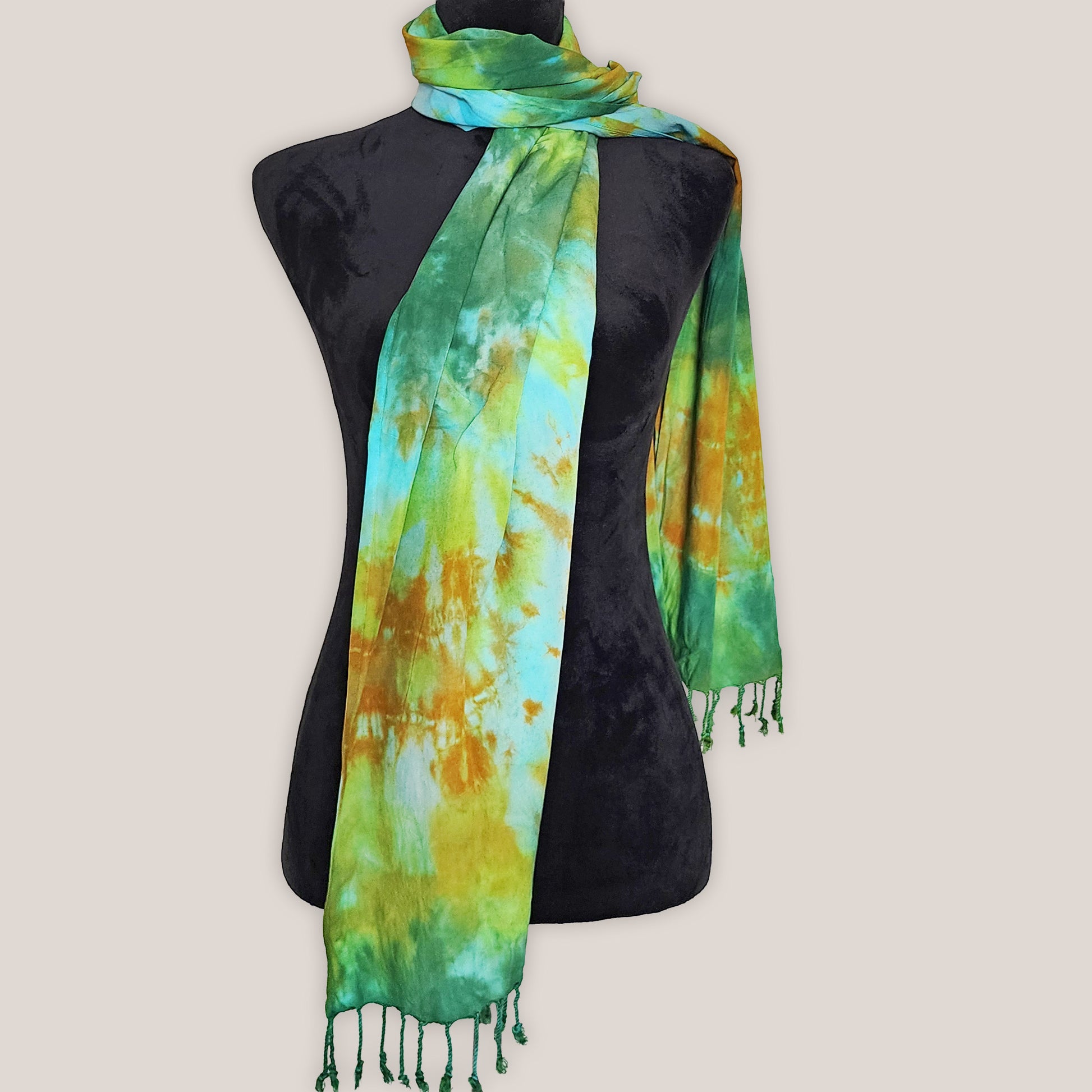 Tie-dye scarf with green and yellow patterns draped over a black mannequin on a light gray background.