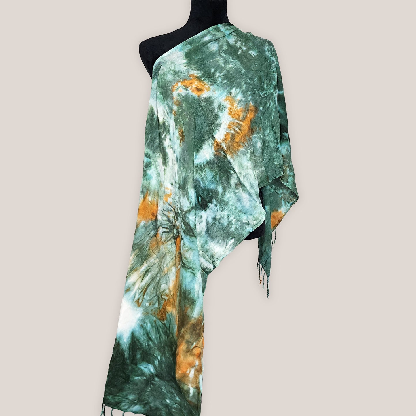 Green and orange tie-dye scarf on a mannequin against a plain background