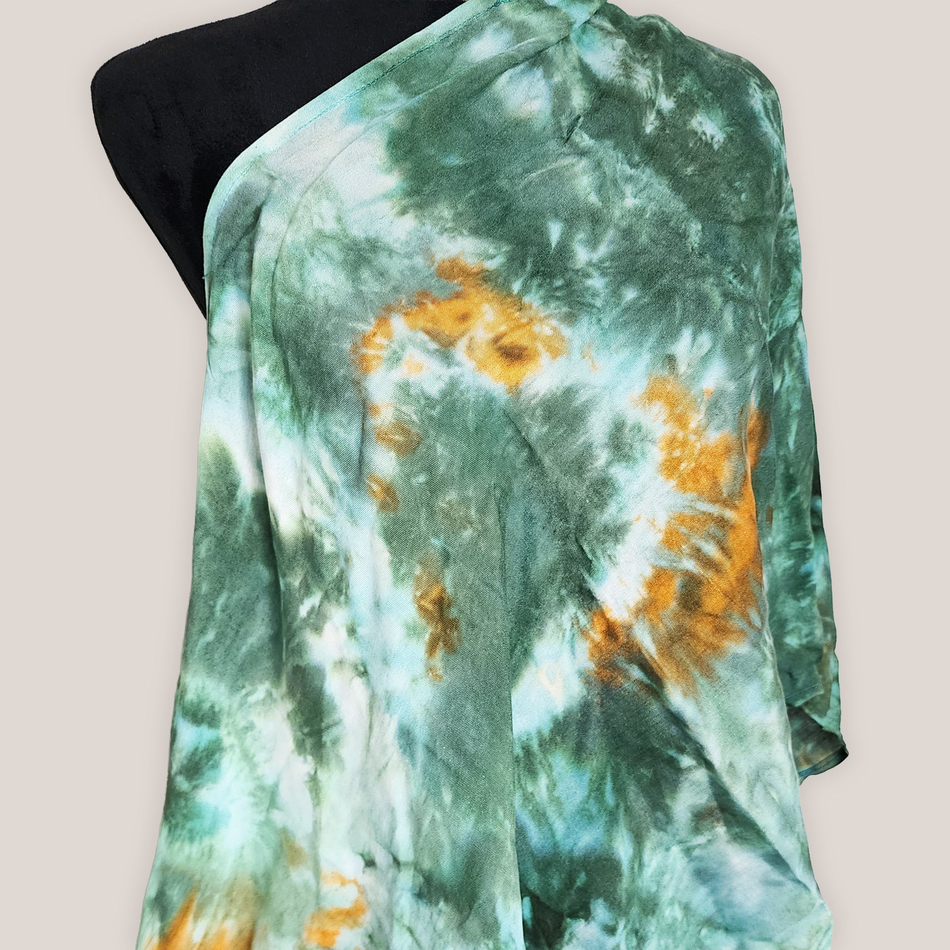 Green and orange tie-dye fabric on a mannequin against a beige background