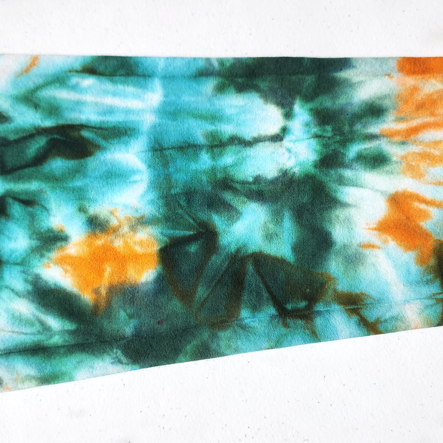 Tie-dye fabric with green and orange pattern on a white background