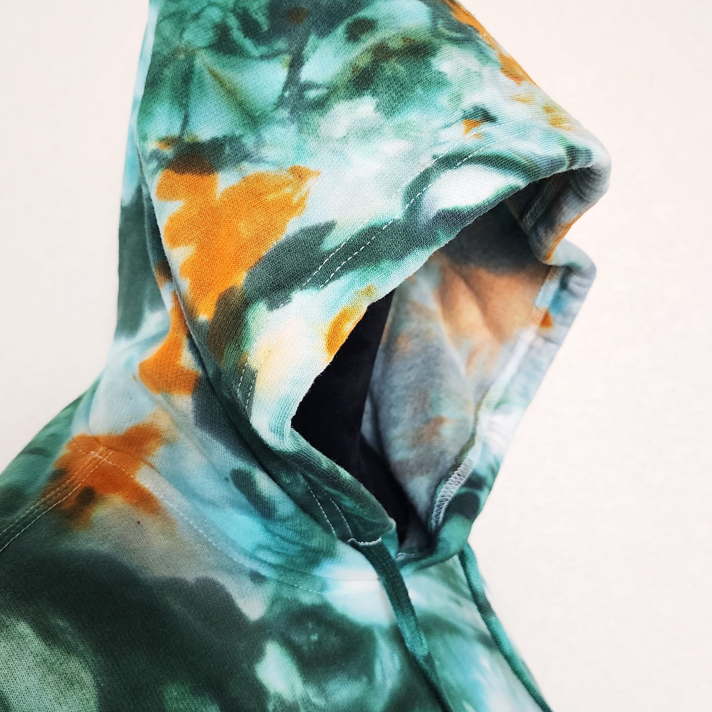 Close-up of a tie-dye hoodie with green and orangecolors on a light background.
