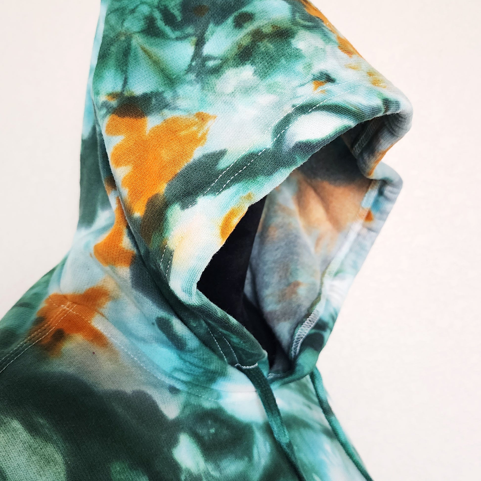 Close-up of a tie-dye hoodie with green and orangecolors on a light background.