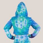 Woman wearing the Galapagos Islands Tie Dye Hoodie Crop Top.  The colors of the crop top include navy blue, teal, aqua, and blue.  Featuring a hood, drawstrings, and raw edge.