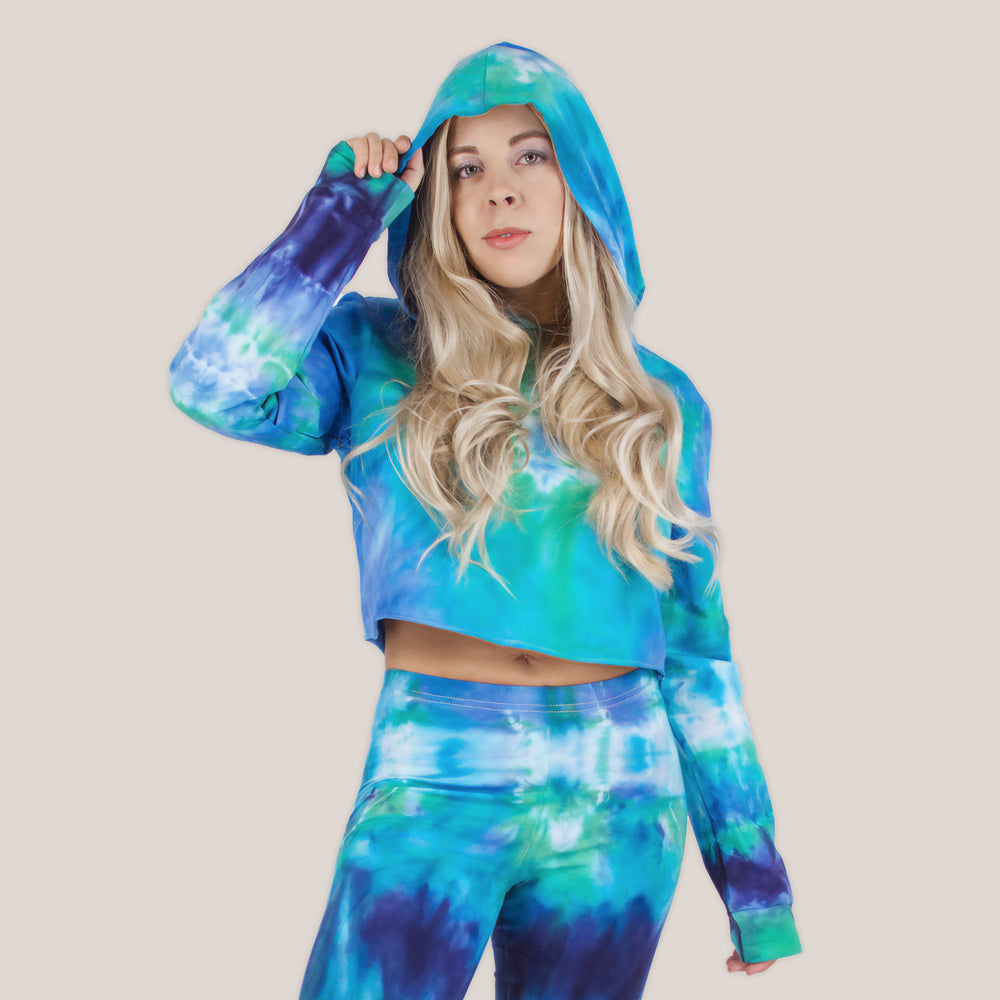 Woman wearing the Galapagos Islands Tie Dye Hoodie Crop Top.  The colors of the crop top include navy blue, teal, aqua, and blue.  Featuring a hood, drawstrings, and raw edge.