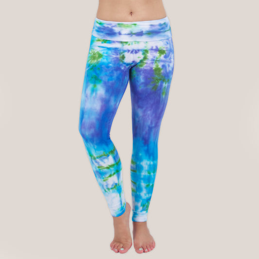 Woman wearing the Grenada tie dye leggings that feature a fold over waistband.  The colors of the leggings include aqua, lavender, and emerald by Akasha Sun