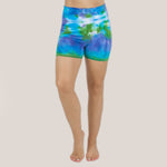 Woman wearing the Grenada tie dye shorts featuring a fold over waistband.  The colors in the shorts include blue, purple, and green by Akasha Sun