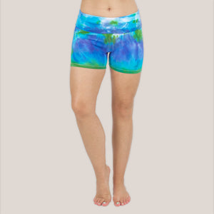 Woman wearing the Grenada tie dye shorts featuring a fold over waistband.  The colors in the shorts include blue, purple, and green by Akasha Sun