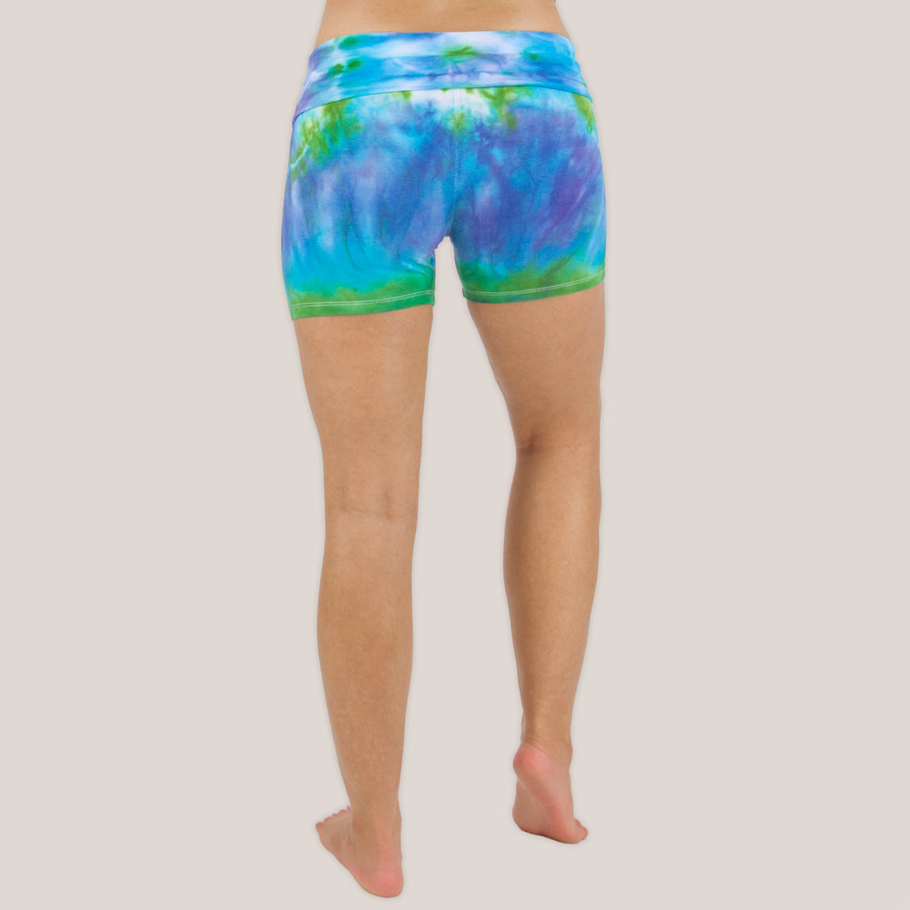 Woman wearing the Grenada tie dye shorts featuring a fold over waistband.  The colors in the shorts include blue, purple, and green by Akasha Sun