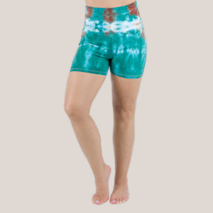 Woman wearing Akasha Sun Kiowa fold over tie dye shorts in teal and brown.