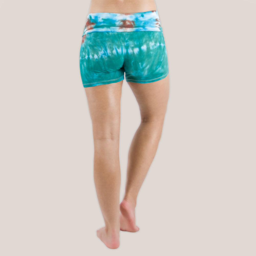 Woman wearing Akasha Sun Kiowa fold over tie dye shorts in teal and brown.