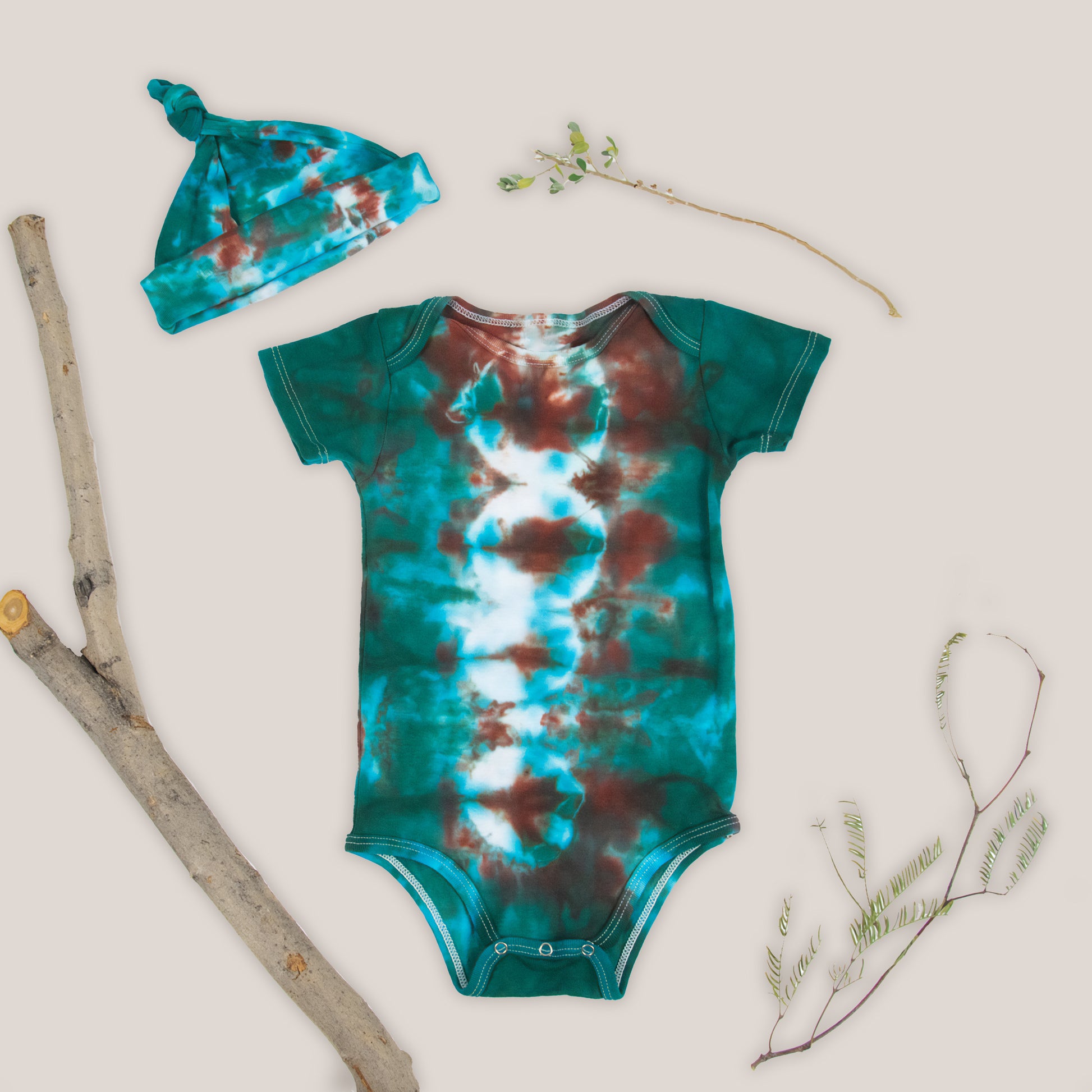 A teal and copper tie dye onesie and baby hat set by Akasha Sun.