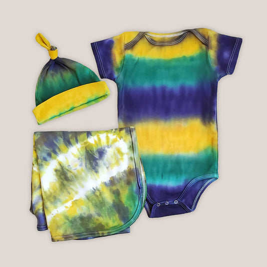 A tie dye organic baby set including a baby blanket bodysuit, hat, and blanket in Mardi Gras colors.