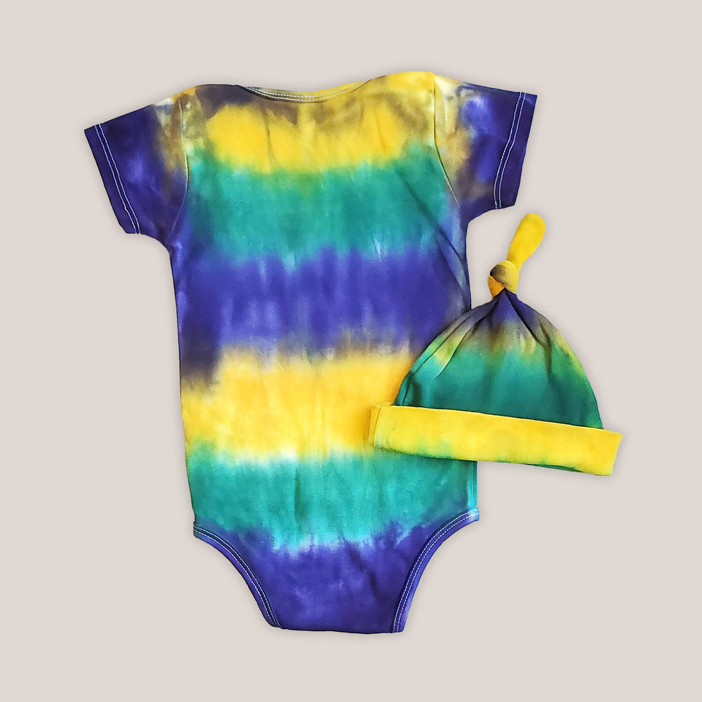 A tie dye organic baby set including a baby blanket bodysuit, hat, and blanket in Mardi Gras colors.