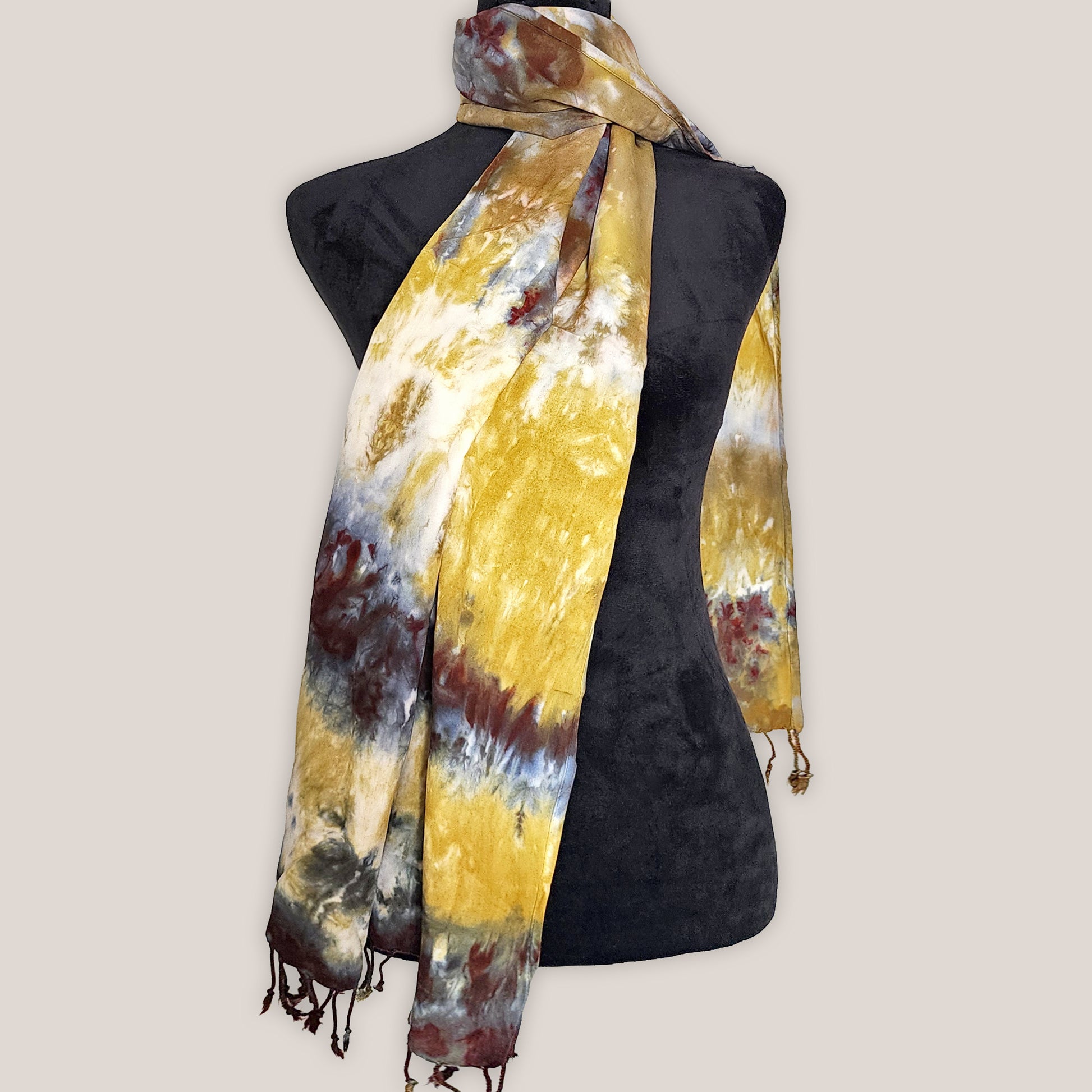 Mannequin wearing a yellow and brown tie-dye scarf on a plain background