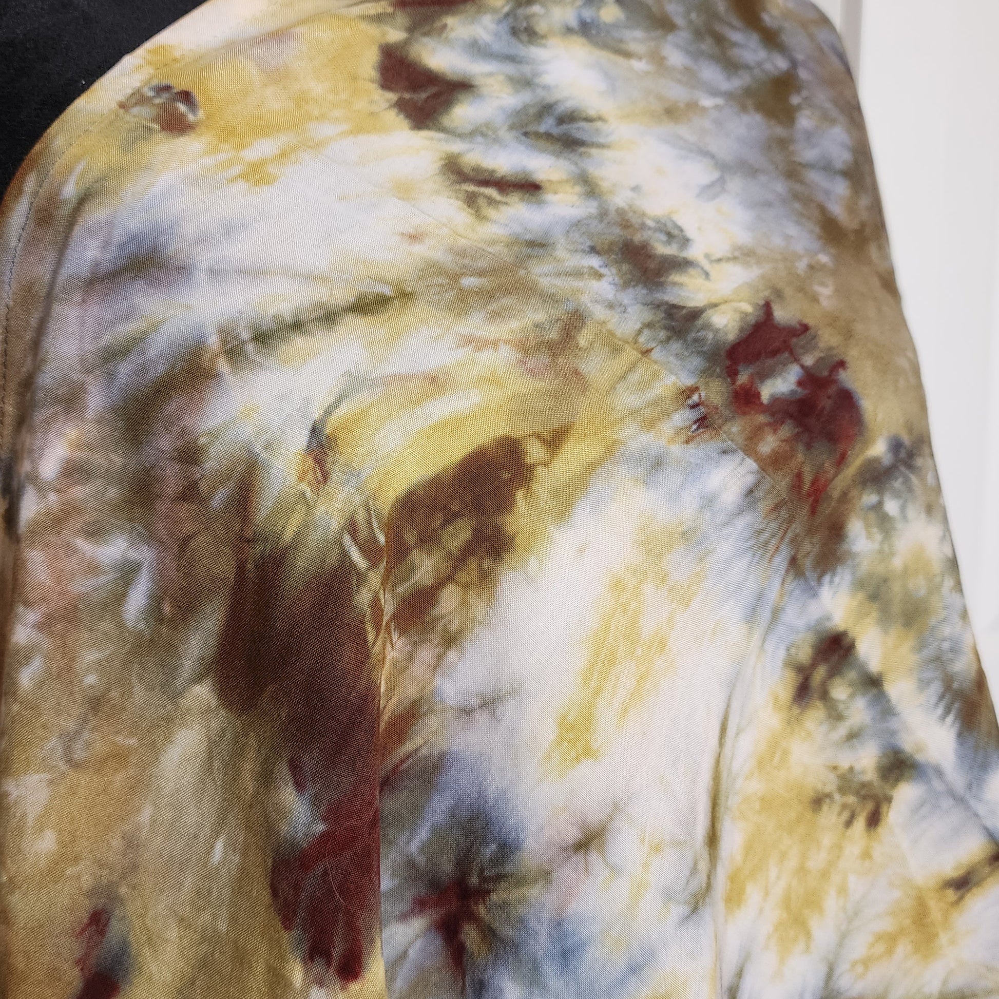 Abstract tie-dye pattern with yellow, brown, and red colors on a fabric surface.