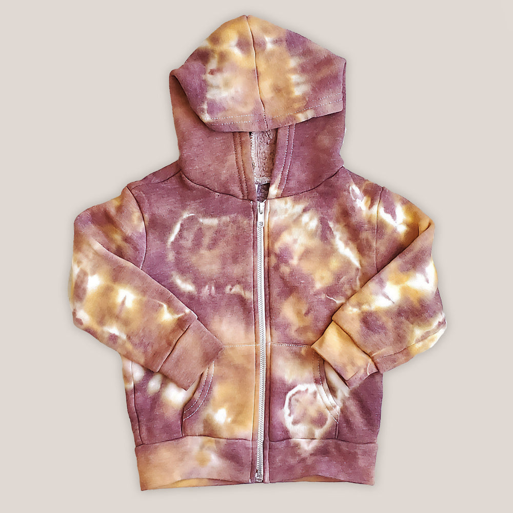 A rust tie dye children's jacket with fleece lining, pockets, and hood.