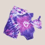 Pink and purple tie dye organic baby set that includes a baby blanket, onesie, and baby hat.