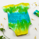 Green, yellow, and blue tie dye organic cotton baby bodysuit and hat set by Akasha Sun.