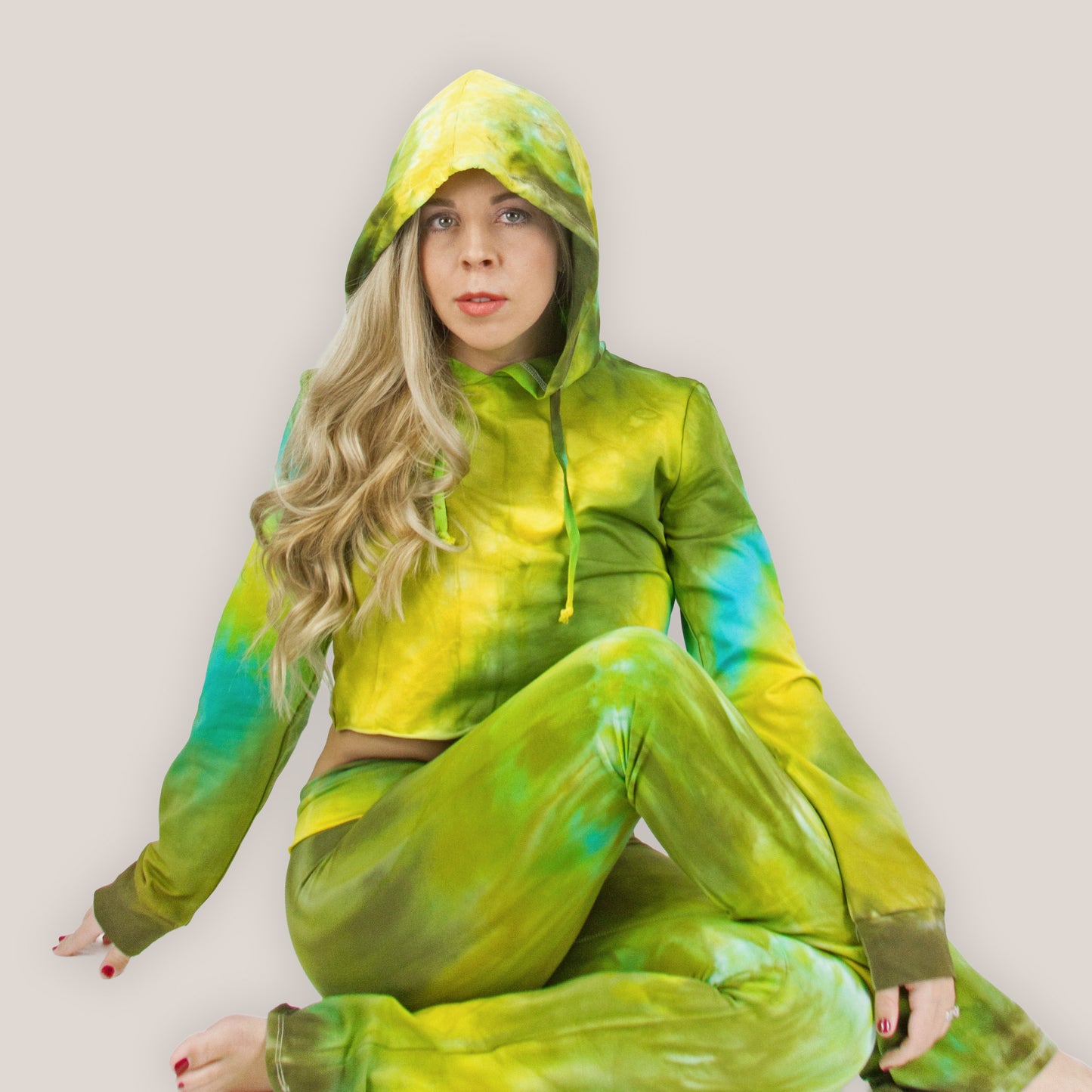 Person wearing a green and blue tie-dye hoodie and pants sitting on a light background