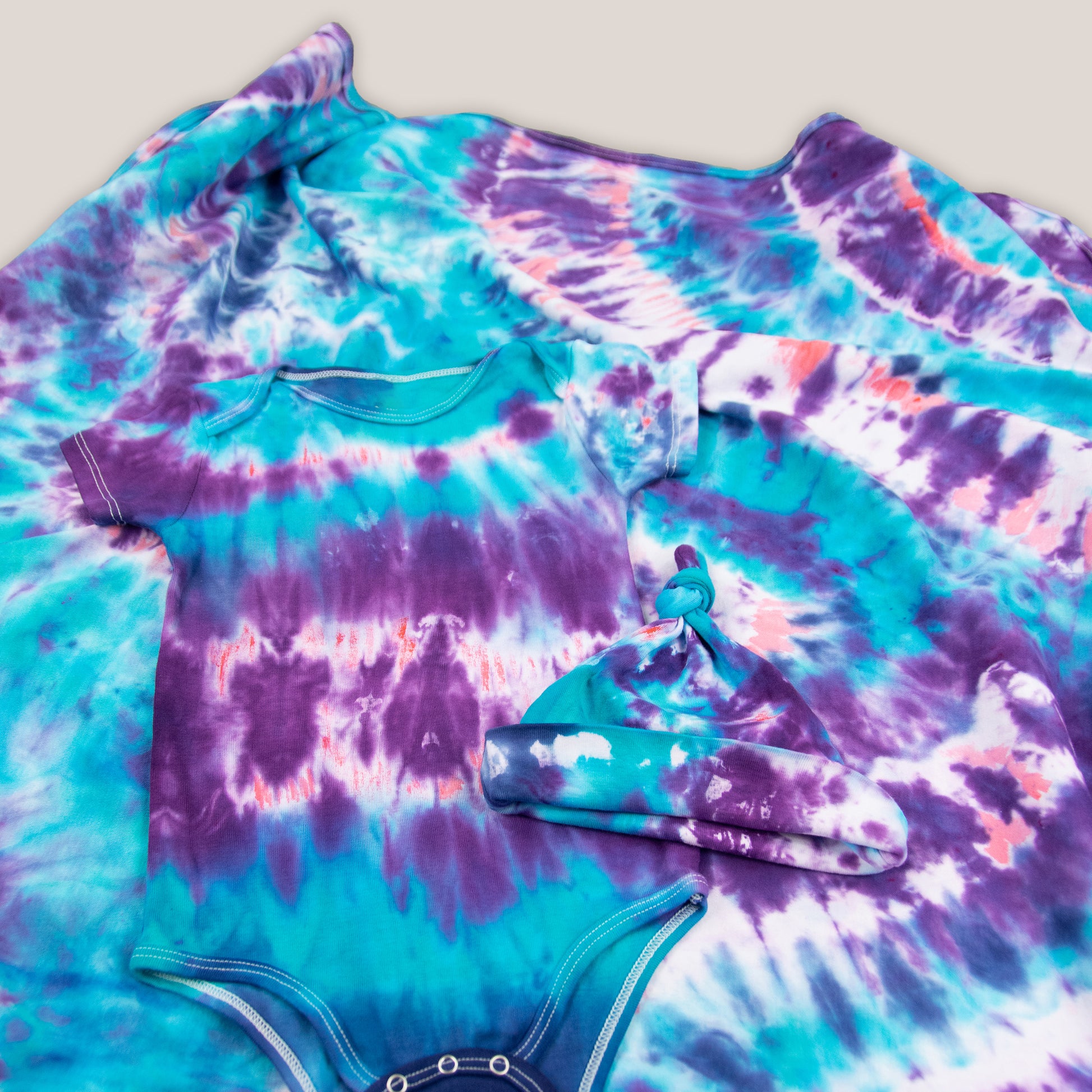 Blue, purple, and pink tie dye baby set that includes a bodysuit, hat, and baby blanket.