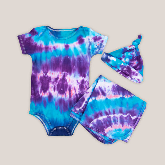 Blue, purple, and pink tie dye baby set that includes a bodysuit, hat, and baby blanket.